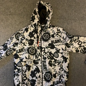 Philipp Plein svartvit vindjacka - Säljer en fet vindjacka från Philipp Plein med svartvit comic-inspirerat mönster och loggor över hela jackan. Jackan har huva med snörning, dragkedja framtill och två sidofickor med dragkedja. Perfekt för dig som gillar att sticka ut med din stil.