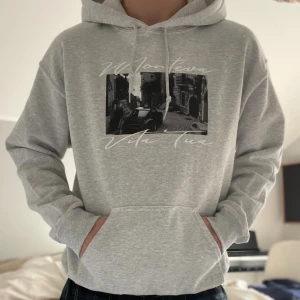 Montévas Limiterade hoodie - Snygg ljusgrå hoodie från Monteva med svartvitt foto-tryck och texten 'Vita Tua' på bröstet. Limited edition kollektionen. Tröjan har huva med snörning och en stor magficka. Perfekt för chill dagar och streetwear-stil.