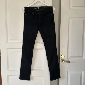 Svarta Roxanne jeans från 7 For All Mankind - Snygga svarta jeans från 7 For All Mankind, modell Roxanne. De har klassisk femficksdesign, smal passform och raka ben. Jeansen är tillverkade i stretchig bomullsdenim för en bekväm känsla och sitter snyggt på kroppen. Vaxad denim med lite shine. 
