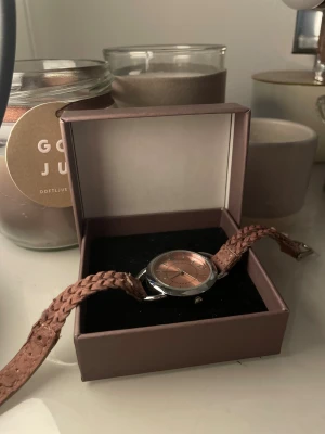 Klocka med flätat rosa skinnarmband - Säljer en stilren klocka med rund urtavla i roséguld och silverfärgad boett. Armbandet är flätat och gjort av rosa skinn, vilket ger en cool och unik look. Perfekt accessoar för dig som vill sticka ut med detaljer och färg.