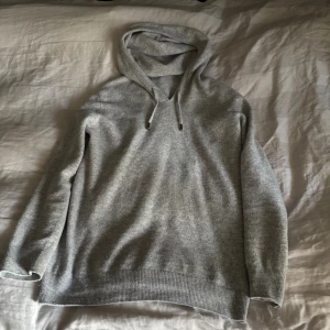 Grå kashmire hoodie  - Fet kashmire hoodie med huva och snörning. Tröjan har långa ärmar och ribbade muddar vid ärmslut och nederkant. Storleken är M 