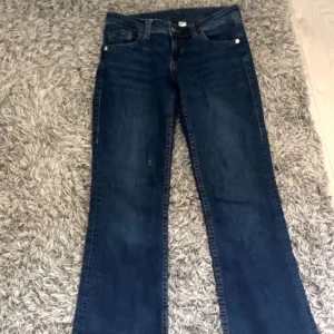 Mörkblå bootcut jeans H&M EUR 34 - Snygga mörkblå jeans från H&M i bootcut-modell med klassiska orange sömmar och femficksdesign. Jeansen är tillverkade i denim och har en normal passform. Perfekta för dig som gillar en tidlös look med lite utsvängda ben.