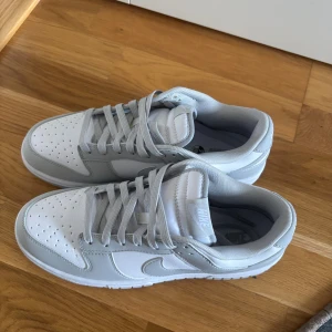 Nike Dunk Low vit/grå sneakers - Nike Dunk Low sneakers i en clean vit och ljusgrå färg. Aldrig anävnda har bara dammat. Strl 42