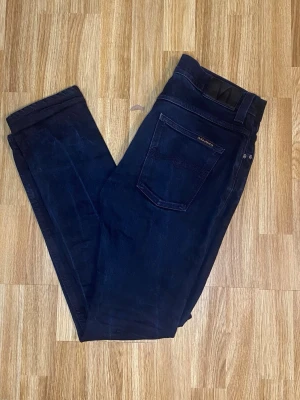 Svarta Nudie jeans grim trin - Snygga svarta Nudie jeans . Klassisk femficksdesign med smal passform och diskreta detaljer. Tillverkade i mjukt och stretchigt jeansmaterial för en bekväm känsla. Perfekta för dig som gillar stilrena och moderna jeans.