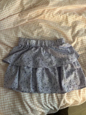 Ljuslila volangkjol från Name It - Supersöt ljuslila kortkjol från Name It med små blommor i mörklila och gult. Kjolen har volangdetaljer och resår i midjan för skön passform. Perfekt för dig som gillar en lekfull och trendig stil.