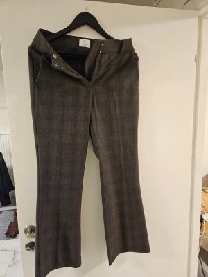 Bruna vida kostymbyxor i ullmix - Snygga bruna kostymbyxor med diskret rutmönster och vida ben. Byxorna har hög midja, hällor för skärp och klassisk knapp- och dragkedjestängning. Perfekta för en dressad look och tillverkade i en mjuk ullblandning.