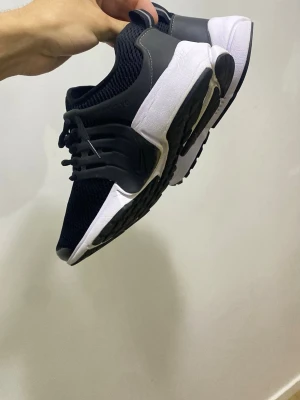 Nike Presto svartvita sneakers - Nike Presto sneakers i svart och vitt med mesh-ovandel för extra andningsförmåga och syntetiska detaljer. Skorna har snörning, platt sula och rund tå. Perfekta för dig som gillar sportig och clean stil.