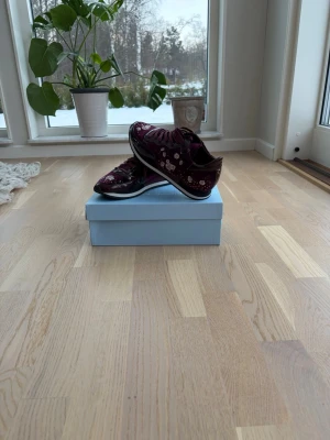 sneakers från Philippe Model - Snygga vinröda sneakers från Philippe Model med  mönster och vita detaljer. Skorna har snörning och en klassisk rund tå. Perfekta för dig som vill sticka ut med stilrena och unika sneakers.