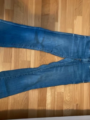 Blå bootcut jeans i klassisk modell - Säljer ett par blå lowwaist bootcut jeans utan fickor på baksidan och normal passform. Jeansen har en snygg tvättad look och är tillverkade i jeansmaterial med bomullskänsla. Perfekta för dig som gillar en tidlös och avslappnad stil. Säljer då jag växt ur dem på längden.