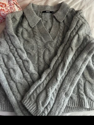 Grå kabelstickad tröja från BikBok - Snygg grå kabelstickad tröja från BikBok med krage och v-ringning. Tröjan har grova flätmönster 