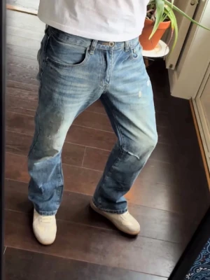 Ljusblåa bootcut jeans - W29/L32 Säljer ett par klassiska jeans i ljusblå tvätt med slitningar och distressed detaljer. Modellen har rak/bootcut passform och normal midja. Från peices of life studio, Jeansen har fem fickor samt knappgylf. Perfekta för en avslappnad och cool stil. Säljer pga inte passar mig.