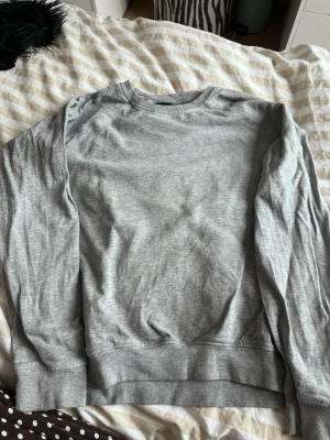 Grå sweatshirt från 157 - En basic grå sweatshirt från 157 med rund halsringning och ribbade muddar vid ärmslut och nederkant. Tillverkad i mjukt material som passar perfekt till en avslappnad stil. Enkel att matcha med jeans eller joggers.