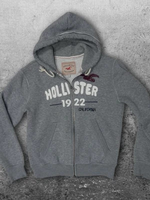 Hollister zip hoodie M - En fet zip hoodie från hollister i storlek M även fast det står XL. Färg grå med vitt tryck. Bra skick! 😀