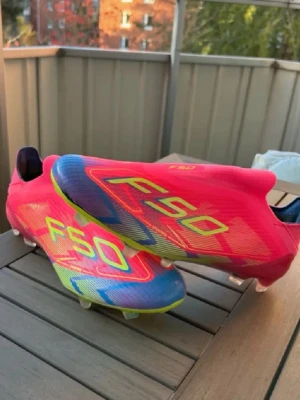 Adidas F50 fotbollsskor rosa/gul elite  - Säljer ett par Adidas F50 fotbollsskor i en riktigt fet färgkombo av rosa, gul och blå. Skorna har en strömlinjeformad design med snörning och platt sula med dobbar för gräsplan. Tillverkade i syntetmaterial för lätt vikt och max speed på planen.