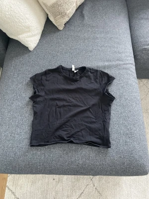 Svart croppad t-shirt - En enkel svart croppad t-shirt med rund hals och korta ärmar. Perfekt basplagg som passar till det mesta och är lätt att styla. Tillverkad i mjuk bomull för en skön känsla.
