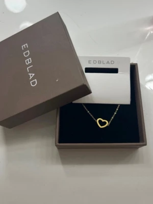 Guldigt hjärthalsband från Edblad - Helt nytt, Snyggt och stilrent halsband från Edblad med ett tunt guldfärgat kedja och ett öppet hjärta som hänge. Perfekt accessoar för att lyfta vilken outfit som helst. Kommer i original ask. Kom privat för exakta mått.