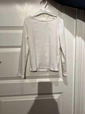 Vit långärmad topp i bomull - En enkel och stilren vit långärmad topp med rund halsringning. Tillverkad i mjuk bomull som känns skön mot huden. Perfekt att matcha med jeans eller kjol för en clean look.