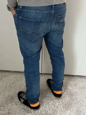 Blå Replay mickym jeans herr - Snygga blå Replay Anbass jeans med klassisk femficksdesign och diskreta slitningar framtill. Jeansen har smal passform och normal midja, tillverkade i mjukt denimtyg som ger en bekväm känsla. Perfekta för dig som gillar en modern och stilren look.