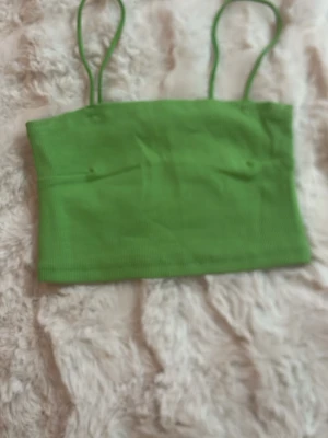 Grön ribbad linnetopp - Snygg grön linnetopp med tunna axelband och ribbad struktur. Perfekt för varma dagar och enkel att matcha med jeans eller kjol. Trendig och enkel design som passar till många olika stilar.