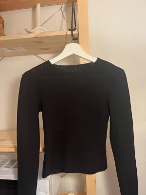 A-DSGN Svart långärmad croppad topp - En svart, långärmad croppad topp med enkel och stilren design. Toppen har en rund halsringning och är tillverkad i ett stretchigt material som sitter tight mot kroppen. Perfekt att matcha med höga jeans eller kjol.