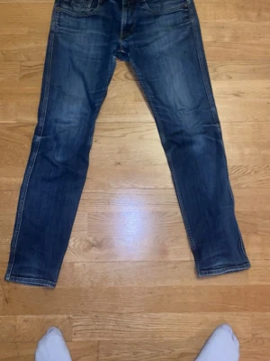 Blå Replay jeans straight fit - Säljer ett par klassiska blå jeans från Replay med raka ben och snygga slitningar. Jeansen har fem fickor, normal passform och detaljerade sömmar på bakfickorna. Perfekta för dig som gillar en tidlös och avslappnad stil.