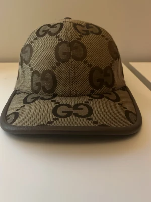 Gucci keps med GG-mönster - Snygg keps från Gucci i beige och brunt med det klassiska GG-monogrammet över hela kepsen. Kepsen har böjd skärm och justerbar rem baktill. Materialet är canvas med läderdetaljer längs kanten för en exklusiv känsla.