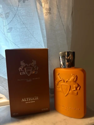 Parfums de Marly Althaïr EdP 125ml - Exklusiv parfym från Parfums de Marly, Althaïr Eau de Parfum. Flaskan är matt orange med silverfärgad kork och har en elegant relief med två hästar och sköld. Kommer i matchande orange kartong. Volym: 125 ml.