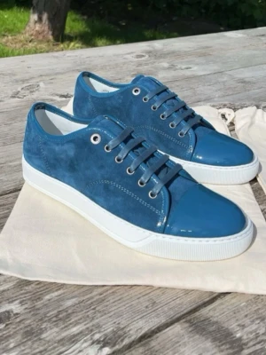 Blå sneakers från Lanvin i mocka och lack - Snygga  blå sneakers från Lanvin med ovandel i mocka och detaljer i blankt lack. Skorna har vita sulor, rund tå och klassisk snörning. Perfekta för dig som vill ha en stilren men ändå unik sneaker med exklusiv känsla.