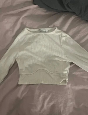 Vit ribbad croppad topp från Newbie - Säljer en vit ribbad croppad topp. Toppen har lång ärm, rund halsringning och är tillverkad i ett mjukt, stretchigt material. Perfekt att styla med höga jeans eller kjol för en clean look.