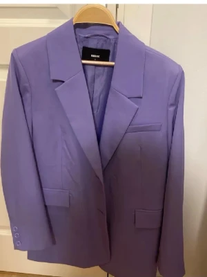 Ljuslila kavaj från Bik Bok - Trendig ljuslila kavaj från Bik Bok med klassisk krage, långa ärmar och knappar vid ärmslutet. Kavajen har en rak passform och flera fickdetaljer framtill. Perfekt för dig som vill sticka ut med färg.