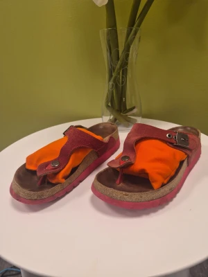 Röda läder sandaler från Scholl, 38 - Unika sandaler med röd mocka. De har en öppen tå, platt sula och spänne i metall på sidan. Sulan är röd och innersulan är i korkliknande material. Perfekta för dig som gillar färg och vill sticka ut.