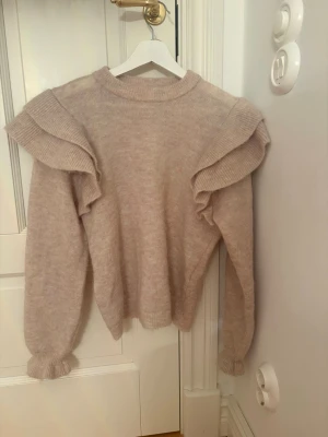 Stickad tröja med volanger  - Jättesnygg beige stickad med volanger på axlarna, den är i väldigt bra skick och är inte nopprig💕