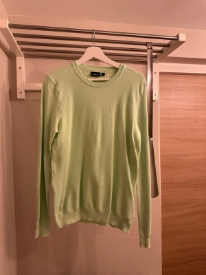 Ljusgrön stickad tröja Sail racing - Snygg ljusgrön stickad tröja från Sail racing med rund halsringning och lång ärm. Tröjan har ett diskret märke på ärmen och är tillverkad i ett mjukt, strukturerat material som känns skönt mot huden. Perfekt sopren look för dig som gillar stilrena plagg.