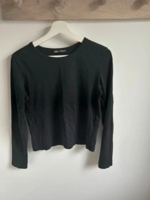 Svart långärmad topp från Zara - En stilren svart långärmad topp från Zara med rund halsringning. Toppen är i ett mjukt bomullsmaterial och har en enkel, klassisk design som passar till många olika outfits.