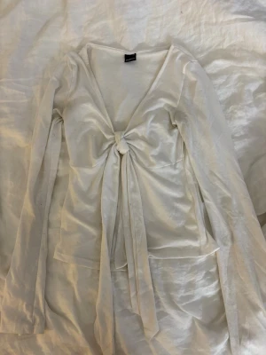 Vit långärmad topp med knyt Gina Tricot - Supersnygg vit långärmad topp från Gina Tricot med djup v-ringning och knyt framtill. Tunn och lätt i materialet, perfekt för lager på lager. Enkel men trendig design som passar till mycket.