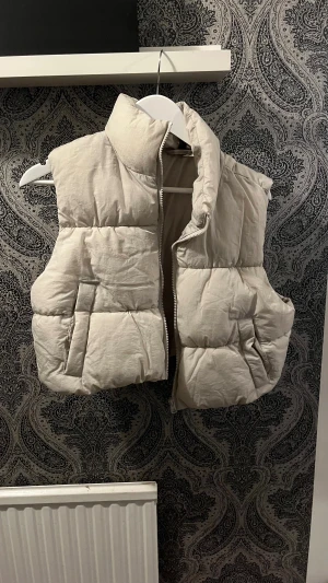 beige väst - En beige väst som har en kort modell med två fickor från H&M 