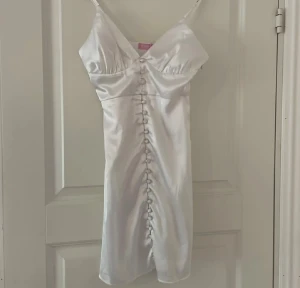 Vit satin klänning med knappar - Säljer en vit klänning i satinmaterial. Klänningen är endast använd fåtal gånger och är i bra skick. Köpt på Nelly från Biancas kollektion.