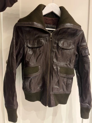 Brun skinnjacka från MNG - Snygg brun skinnjacka från MNG Casual Sportswear med bred ribbad krage och muddar. Perfekt för dig som gillar en cool och tidlös stil. 