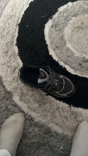 Svarta Asics sneakers strl 40.5 - Säljer ett par svarta Asics sneakers med grå och vita detaljer. Skorna har mesh och syntetmaterial på ovansidan, snörning och en platt sula. Perfekt för dig som gillar sportig stil och vill ha bekväma skor till vardagen.