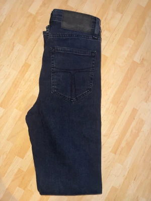 Mörkblå skinny jeans från Tiger of Sweden  - Snygga mörkblå skinny jeans från tiger of Sweden  med klassisk femficksdesign och svarta detaljer på bakfickan. Jeansen har smal passform och är tillverkade i stretchigt denim för extra komfort. Perfekt för dig som gillar en modern och stilren look.