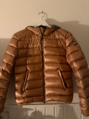 Colmar roséguldig dunjacka med huva - Säljer en roséguldig, glansig dunjacka från Colmar med huva och dragkedja framtill. Jackan har två snedställda fickor med dragkedja och quiltad design. Perfekt för kalla dagar och riktigt snygg färg som sticker ut.