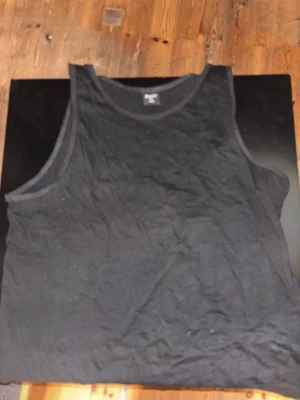 Svart linnetopp från Basic XL - Svart enkel linnetopp från Basic i storlek XL. Modellen är ärmlös med rund halsringning och har en loose passform. Perfekt för dig som gillar minimalistisk stil och vill ha något bekvämt och lätt att matcha. Materialet känns mjukt och passar till många olika looks.