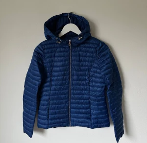 Blå pufferjacka från Massimo Dutti - Säljer en marinblå pufferjacka från Massimo Dutti i storlek S. Jackan har huva med snörning, quiltad design och dragkedja framtill. Materialet är syntet och jackan är perfekt för kyliga dagar. Stilren look som funkar till många outfits. 5N10