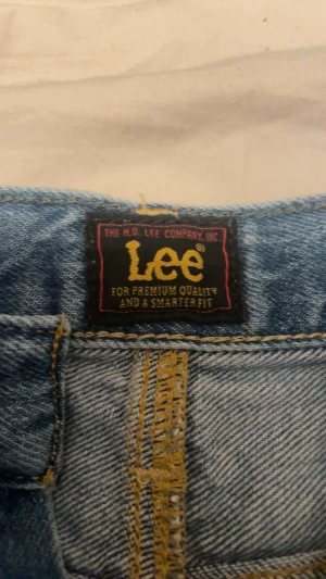 Blå jeansshorts från Lee - Säljer ett par klassiska blå jeansshorts från Lee med fem fickor, knappgylf och snygga kontrastsömmar. Shortsen har en rak passform och är tillverkade i slitstark bomullsdenim. Perfekta för en chill sommarstil.