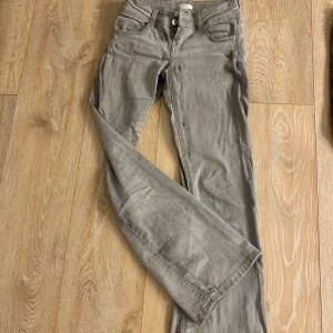 Grå bootcut, lågmidjade jeans - Snygga grå jeans med bootcut-snitt och klassisk femficksdesign. Byxorna har normal passform och är tillverkade i mjukt jeanstyg med dragkedja och knappstängning. Perfekta för dig som gillar en avslappnad stil med lite extra vidd vid benslutet. Lågmidjade