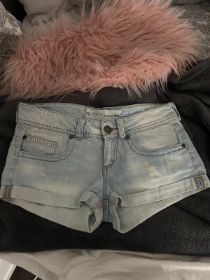 Ljusblå jeansshorts Victoria’s secret Forever Pink - Säljer ett par ljusblå denimshorts från Forever Pink i storlek XS. Shortsen har låga midja, slitna detaljer och glittriga strass på fickor och hällor. Klassisk femficksmodell med uppvikta benslut och snygga kontrastsömmar. Perfekt för dig som gillar bling och streetstyle.