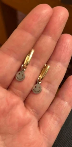 örhängen med smiley-berlocker - Charmiga örhängen med små glada smiley-anhängare i silverfärgat stål. Fästen i guldfärg som ger en fin kontrast och ett modernt uttryck. Perfekt till vardag eller som en rolig detalj till fest! Man kan ta bort smiley