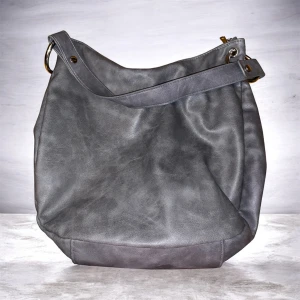 Grå axelväska i skinn - Stilren grå axelväska i mjukt skinn med enkel design och bred axelrem. Väskan har metallringar i sidorna och en rymlig insida, perfekt för att bära med sig allt man behöver under dagen.