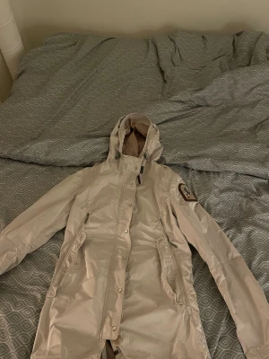 Beige vindjacka från Parajumpers S - Snygg beige vindjacka från Parajumpers med huva, dragkedja och tryckknappar. Jackan har två stora fickor med dragkedja och klassisk PJS-patch på ärmen. Perfekt för blåsiga dagar och har meshfoder för extra ventilation.