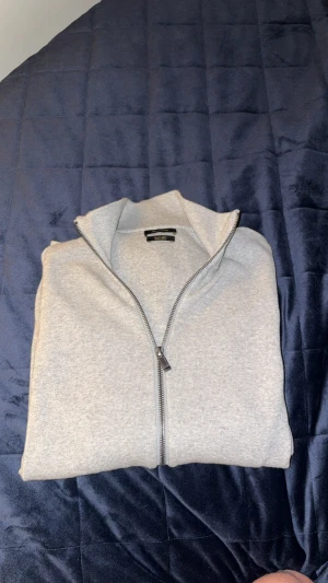 Ljusgrå kofta från Massimo Dutti - Säljer en stilren ljusgrå kofta från Massimo Dutti med hel dragkedja framtill. Tröjan är i mjuk bomullsmix och har en hög krage som ger en clean look. Perfekt för lager-på-lager och passar till allt. Tröjan är helt som ny och endast använd 1 gång, nypris 1200, mitt pris 500!